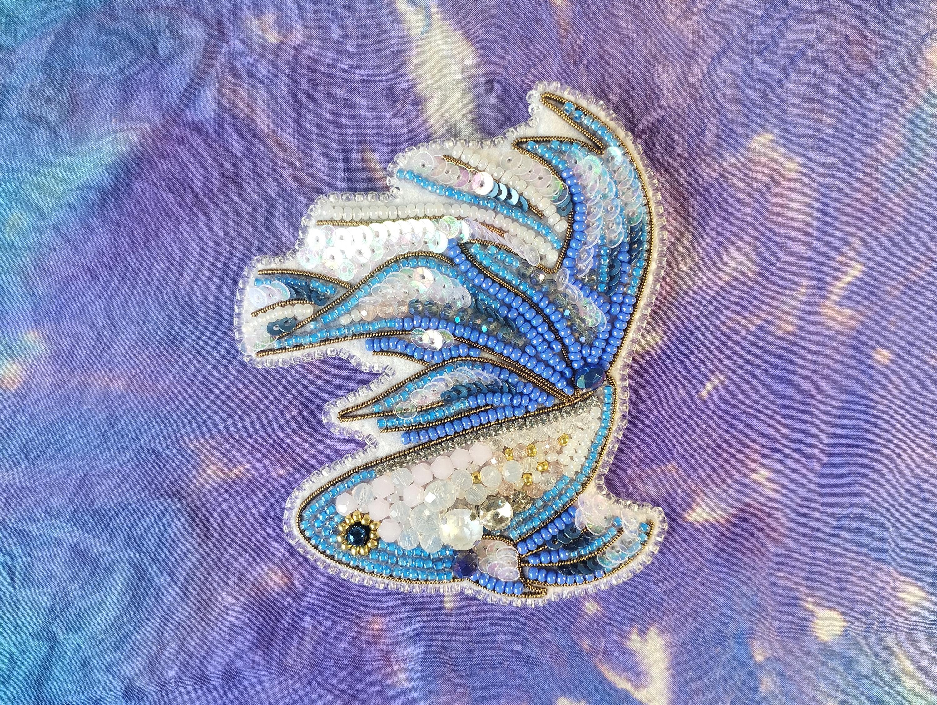 a decorative piece of embroidered or beaded art, with a blue and white color scheme, placed on a textured purple background.